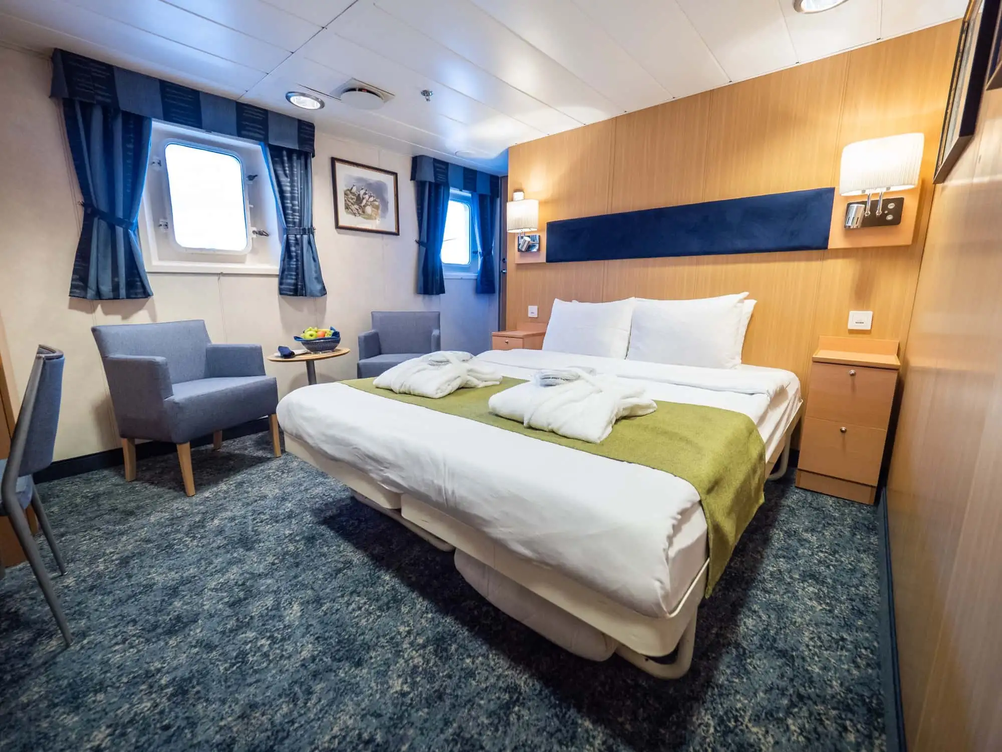 The Owners cabin (1) has a double bed, two large viewing windows, cabinets, wardrobes, separate sitting area, desk, TV,  and a private bathroom with shower and toilet. – Norwegian Adventure Company