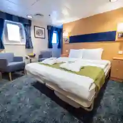 The Owners cabin (1) has a double bed, two large viewing windows, cabinets, wardrobes, separate sitting area, desk, TV,  and a private bathroom with shower and toilet. – Norwegian Adventure Company
